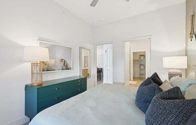 A bedroom with a large bed and a dresser with a lamp on top.