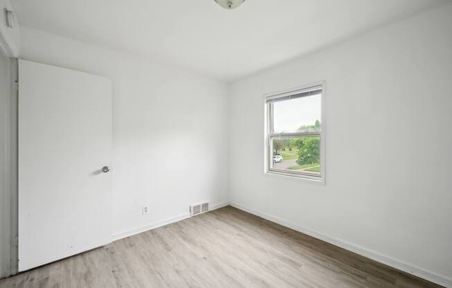 A room with a white door and a window with a view of a street.
