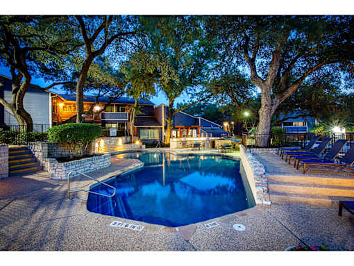 A pool surrounded by a stone wall and trees at night.