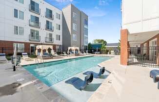 A pool with a slide and sun loungers in front of apartment buildings.