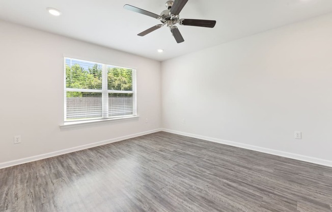 an empty living room with a ceiling fan and a window