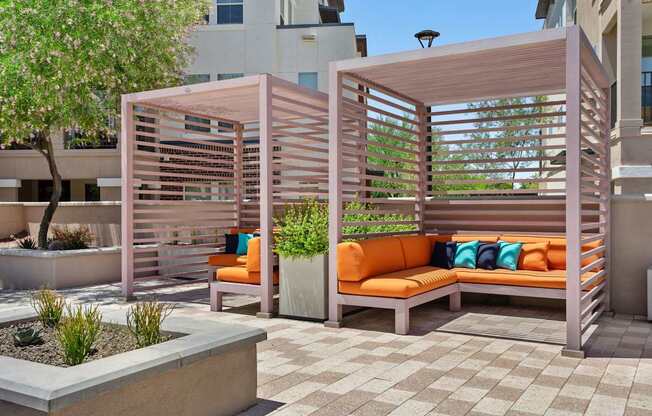 A wooden bench with orange cushions is situated under a wooden trellis.