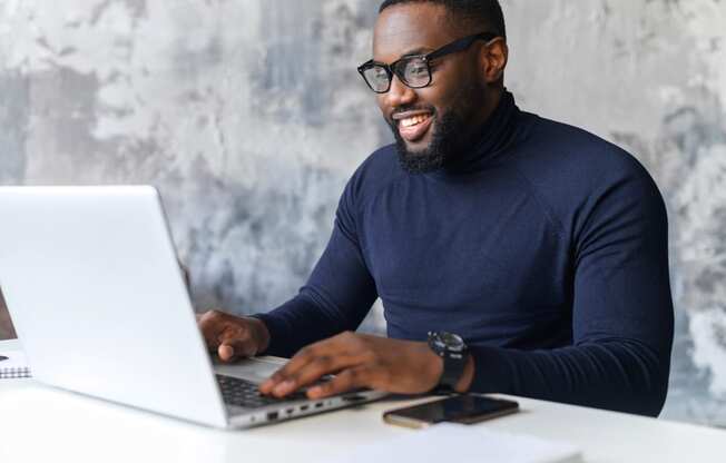 a man sitting at a table using a laptop computer at The Crest at South Point, McDonough, 30253