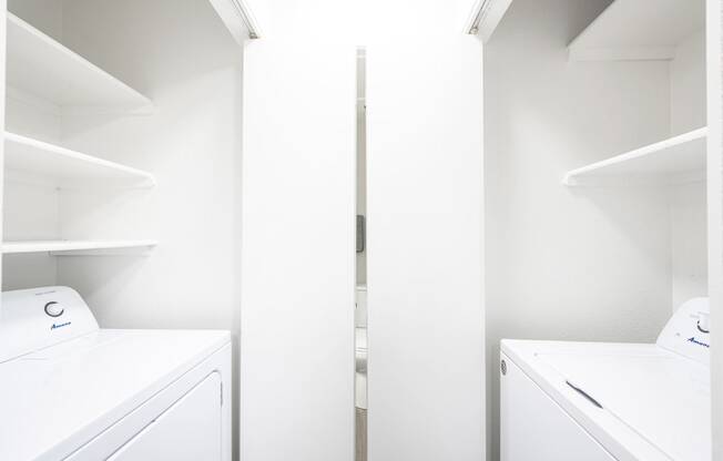 a washer and dryer in a laundry room with white walls and white shelves