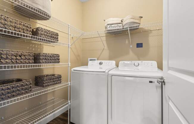 A laundry room with two washing machines and shelves with baskets on them.