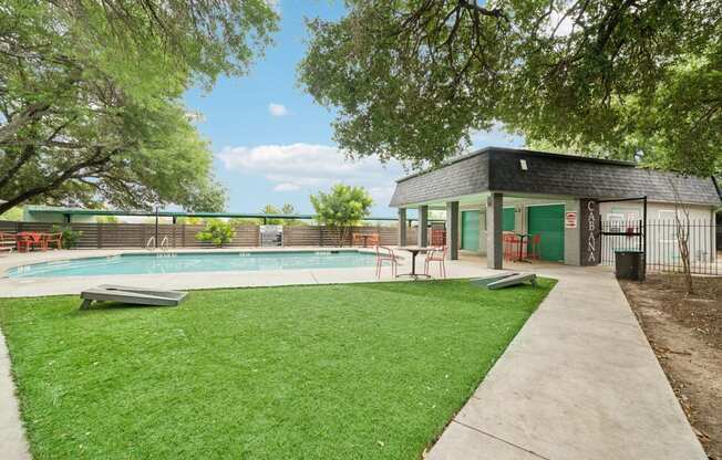 a pool with a pavilion and a grassy area with trees and a building