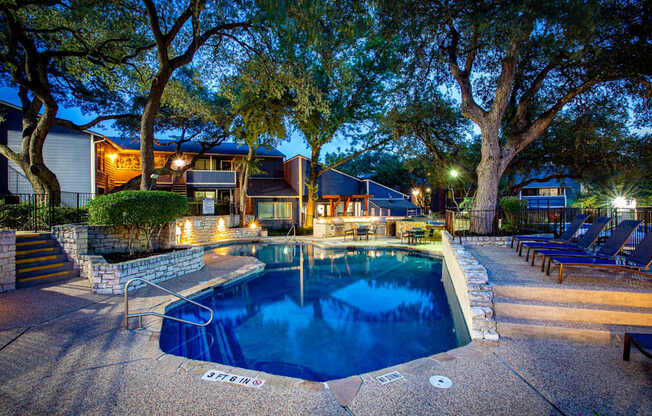 A pool surrounded by a stone wall and trees at night.