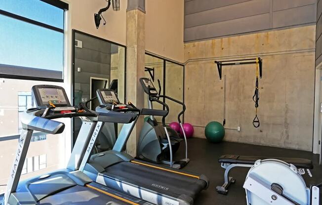 a gym with treadmills and weights in a building with a large window