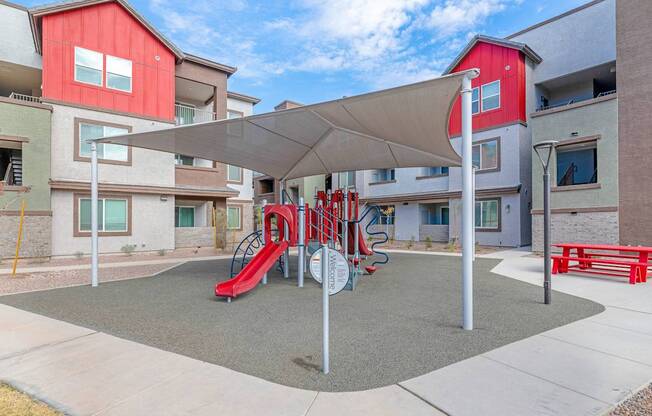 A playground with a red slide and a grey canopy.