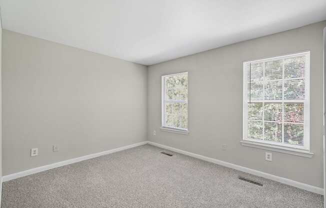 A room with a carpeted floor and two windows with blinds.