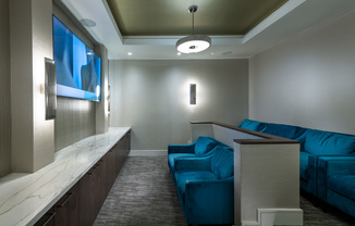 Theater with two elevated rows of plush blue upholstered loveseats facing a large HDTV screen.