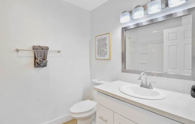 A white bathroom with a toilet, sink, mirror, and a towel rack at Verandas Apartments, West Covina, 91791