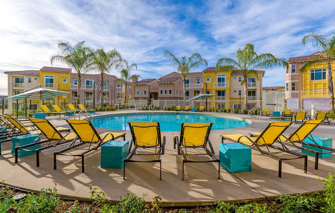 A pool surrounded by yellow chairs and palm trees.