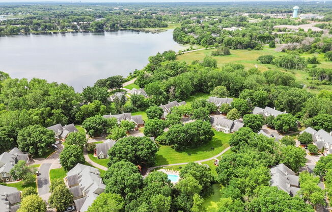 A bird's eye view of a residential area with houses surrounded by trees and a lake in the background.