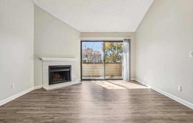 A large, empty room with a fireplace and sliding glass doors leading to a balcony.