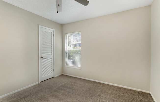 A room with a carpeted floor, a ceiling fan, and a window with blinds.
