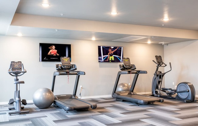 two treadmills and exercise balls in a gym with televisions