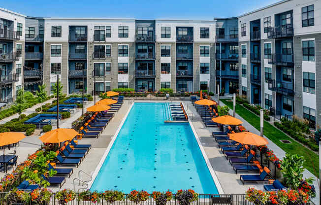 an outdoor pool with orange umbrellas in front of an apartment building