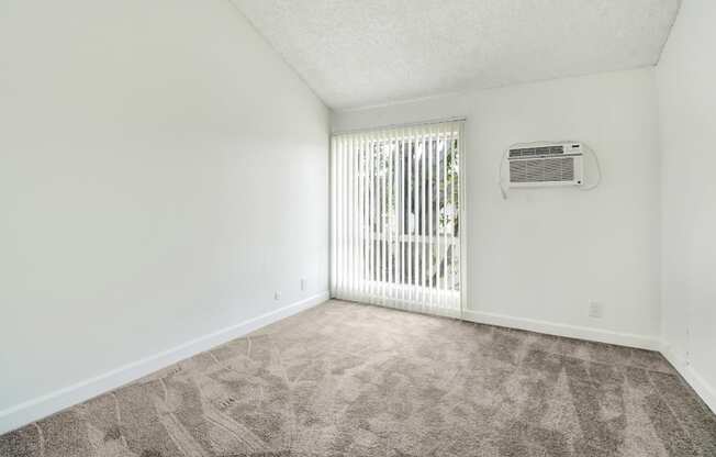 A room with a carpeted floor and a window with blinds.