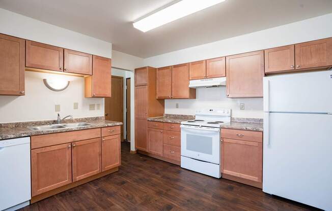 A kitchen with wooden cabinets and white appliances. Fargo, ND Birchwood 2 Apartments
