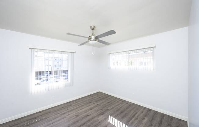 an empty bedroom with a ceiling fan and two windows