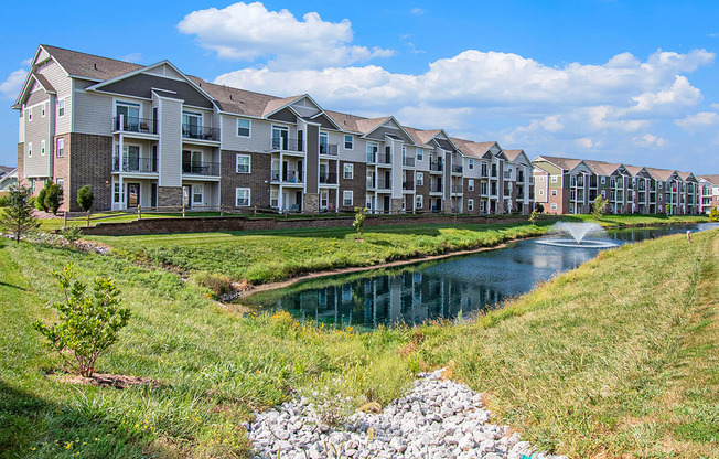 A row of apartments next to a pond with a fountain at Strathmore Apartment Homes, West Des Moines, IA