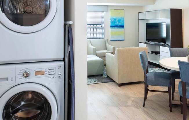 a living room with a washing machine and a kitchen with a table and chairs at Parks Residential - Denver, Centennial Colorado