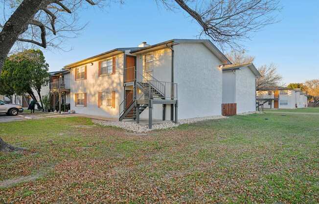 A white house with a brown door and a tree in front.