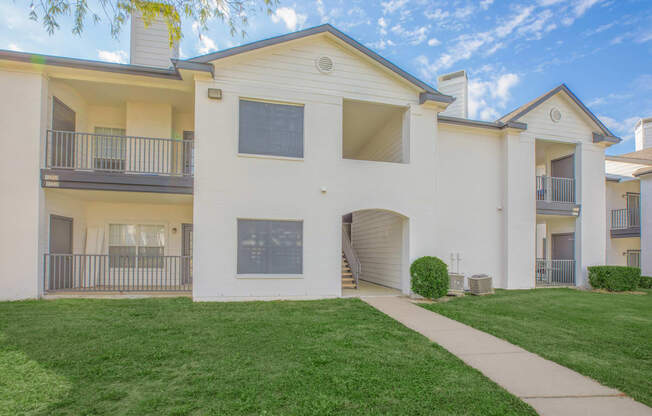 a white apartment building with a green lawn and a sidewalk