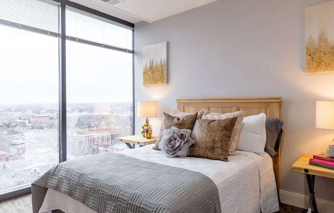 A bedroom with a large window overlooking a cityscape.