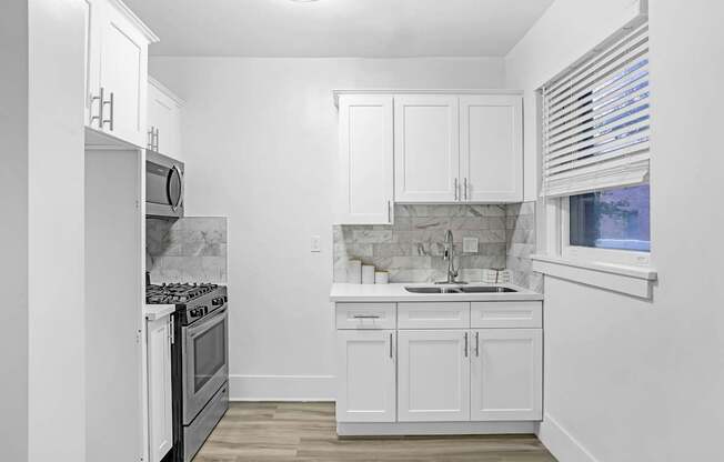 A kitchen with white cabinets and a marble backsplash.