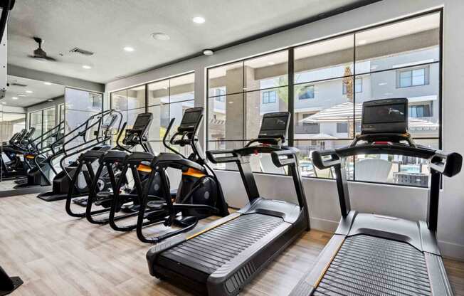 a gym with cardio equipment and large windows
