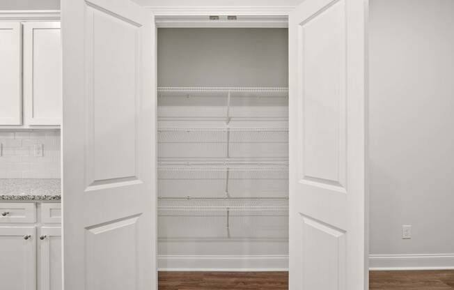 a pantry with white cabinets and white walls and a wood floor