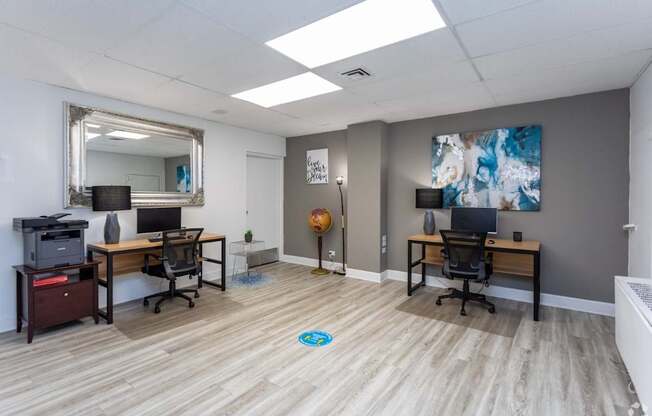 A room with two desks and a printer on a cabinet.