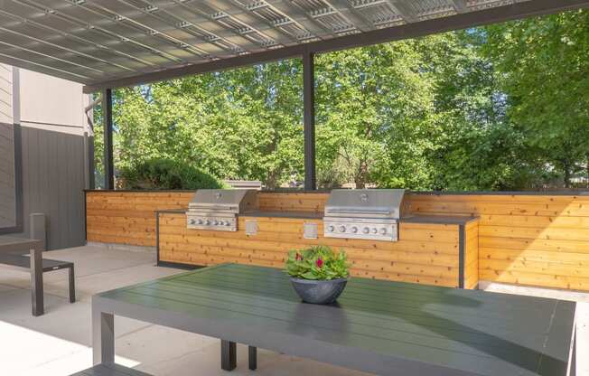 an outdoor kitchen with two bbq grills and a table with a potted plant