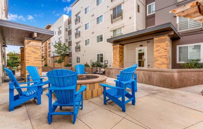 a patio with blue chairs and a fire pit in front of an apartment building at Parks Residential - Denver, Centennial