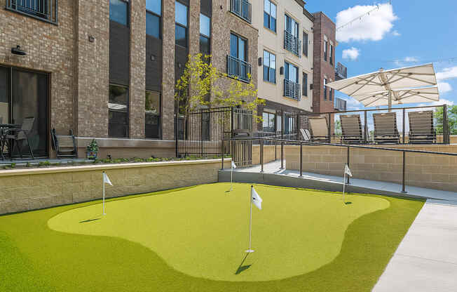 A small putting green is surrounded by a brick building.