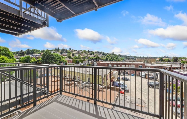 A balcony with a metal railing overlooks a parking lot and buildings.