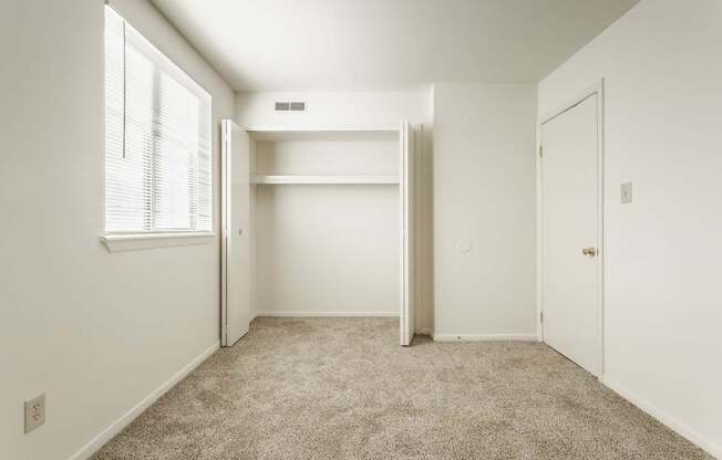 A white bedroom with a window and a carpeted floor.