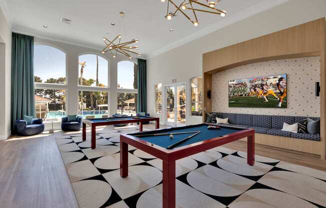 a billiards room with two pool tables and a tv in front of windows
