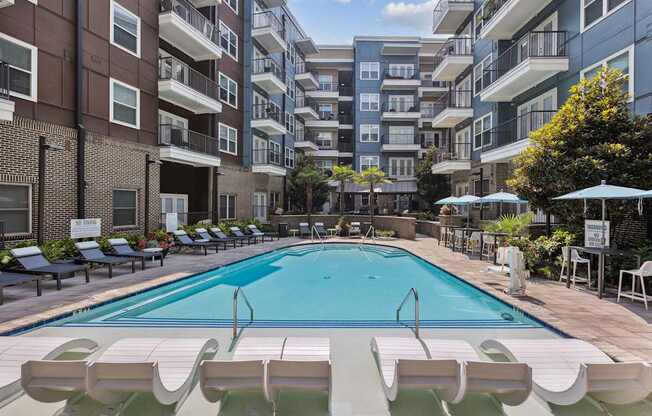 an outdoor swimming pool with lounge chairs and umbrellas in front of an apartment building