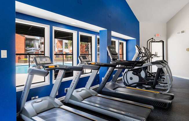Fitness center with treadmills, ellipticals, and large windows overlooking the pool courtyard.