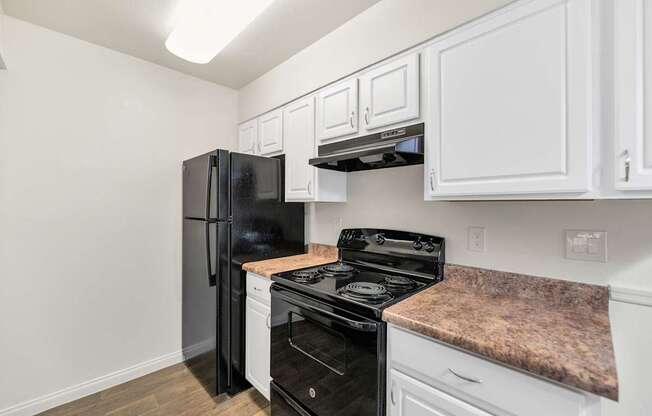 A black fridge and stove in a kitchen with white cabinets at Urban WalkApartments on 6th Avenue, Arizona 85016