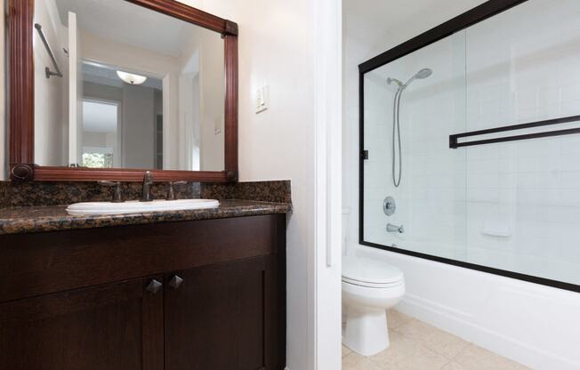 Palo Alto, CA Apartments For Rent - Bathroom With Large Mirror, Sink, Dark Brown Cabinets, Toilet, And Glass Sliding Door Shower With Tub