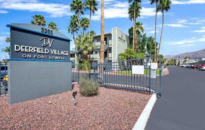 A sign for Deerfield Village on Fort Lowell stands in front of a building and palm trees.