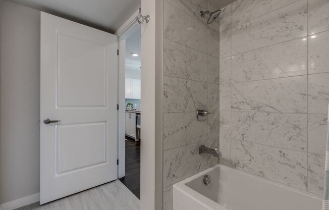 Lux Apartments Bellevue bathroom with floor to ceiling tiling in the bathtub and shower, and light-grey wood-style vinyl flooring