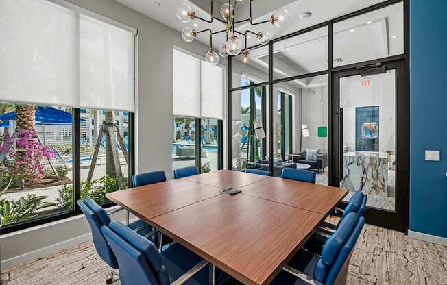 A conference room with a long table and chairs, a chandelier, and a view of the outside through the windows.