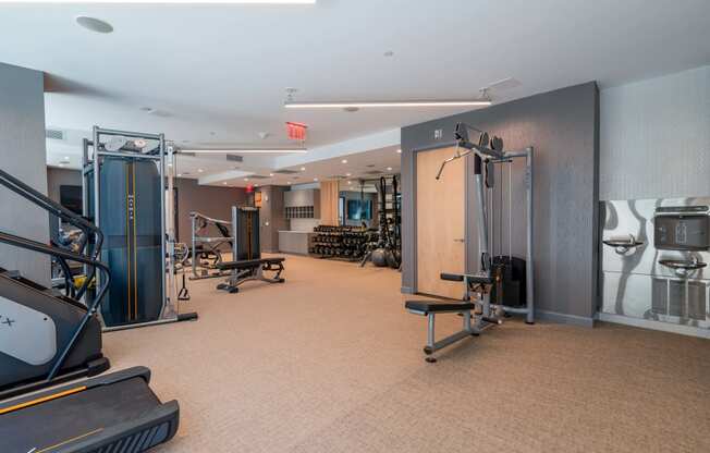 a gym with weights and cardio equipment on the floor and a mirrored wall