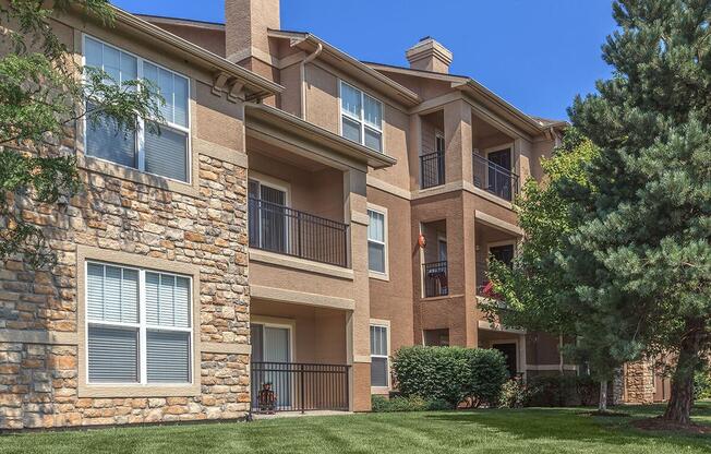 The exterior of an apartment building overlooking a lush green space and tree