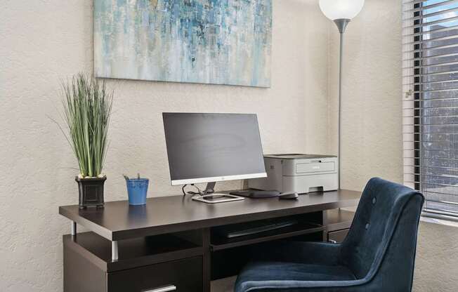 A blue cup sits on a desk with a monitor, printer, and lamp.